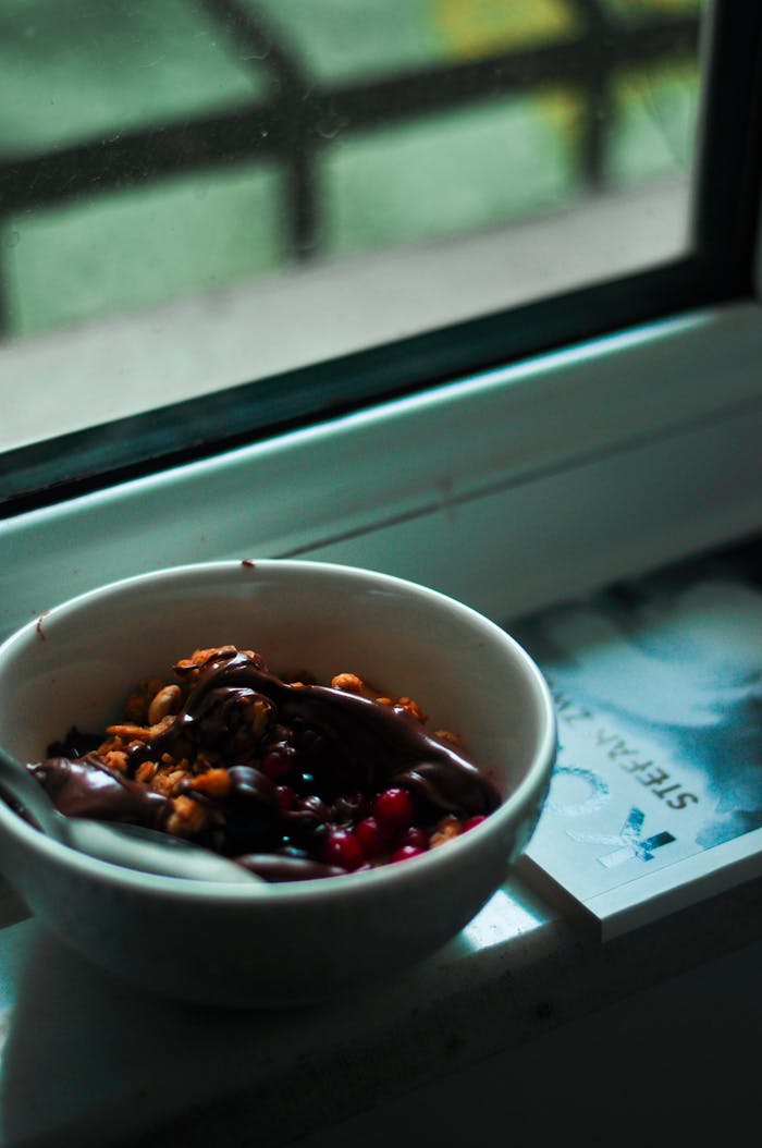 Delicious breakfast bowl featuring nuts and berries beside a window sill.